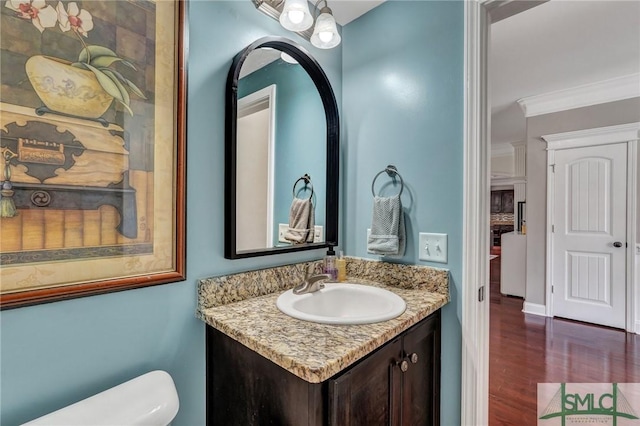 half bath featuring vanity, crown molding, toilet, and wood finished floors