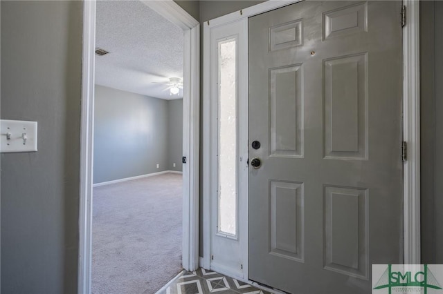 carpeted entrance foyer featuring baseboards, visible vents, a textured ceiling, and ceiling fan