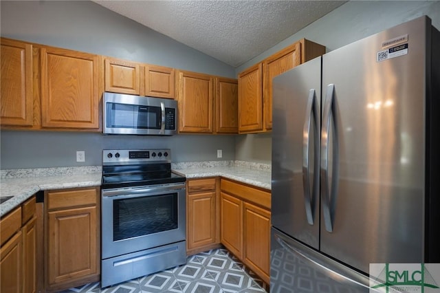 kitchen with brown cabinets, a textured ceiling, stainless steel appliances, light countertops, and vaulted ceiling