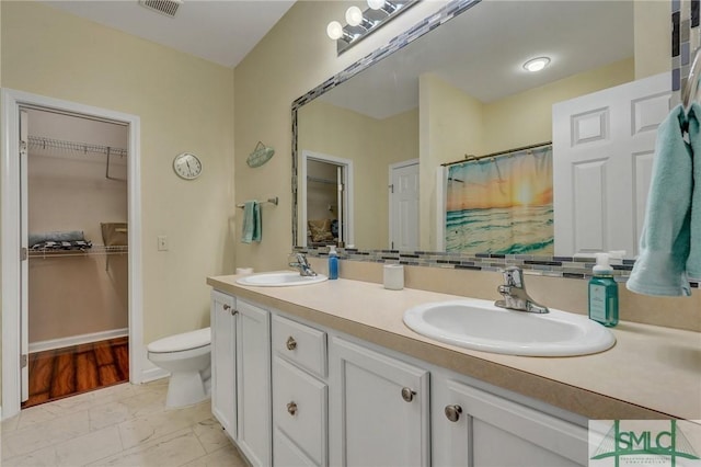 full bath with a walk in closet, double vanity, toilet, and a sink