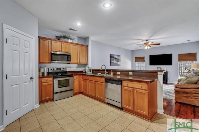 kitchen with a peninsula, a sink, appliances with stainless steel finishes, dark countertops, and open floor plan