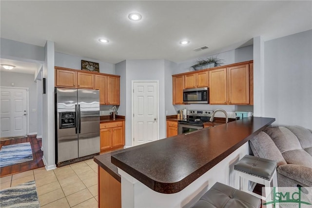 kitchen featuring dark countertops, visible vents, light tile patterned floors, a peninsula, and stainless steel appliances