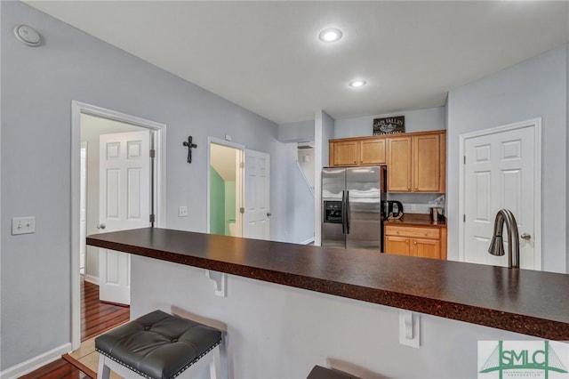 kitchen featuring dark countertops, baseboards, a kitchen bar, recessed lighting, and stainless steel refrigerator with ice dispenser