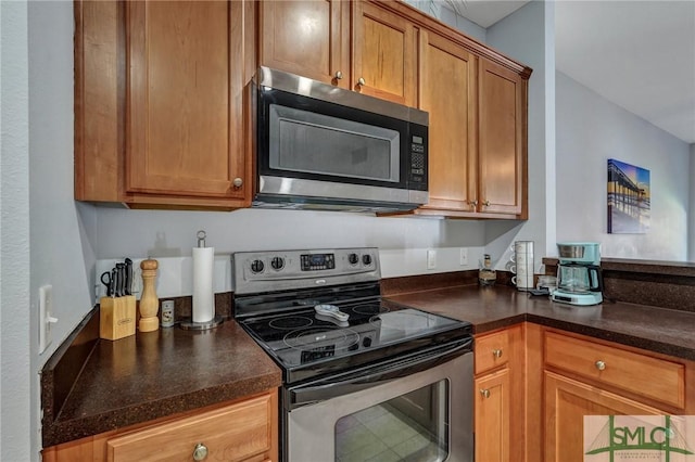 kitchen featuring stainless steel appliances, dark countertops, and brown cabinetry