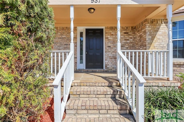 view of exterior entry with a porch and brick siding