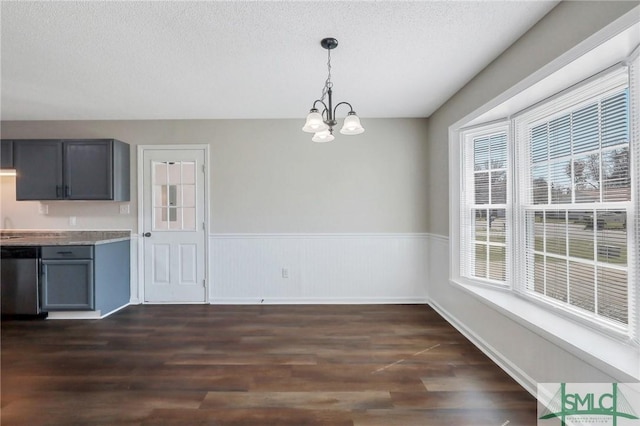 unfurnished dining area with a textured ceiling, dark wood-style flooring, a chandelier, and wainscoting