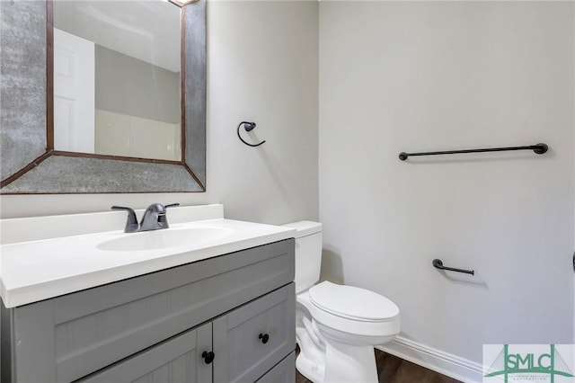 bathroom featuring baseboards, toilet, wood finished floors, and vanity