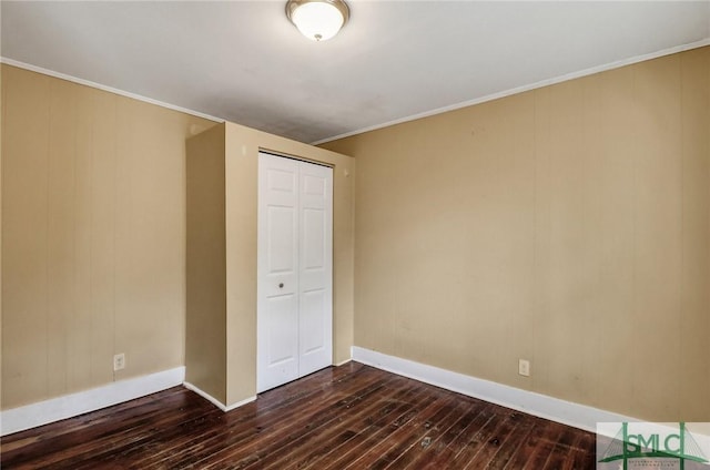 unfurnished bedroom with dark wood-type flooring, baseboards, a closet, and ornamental molding