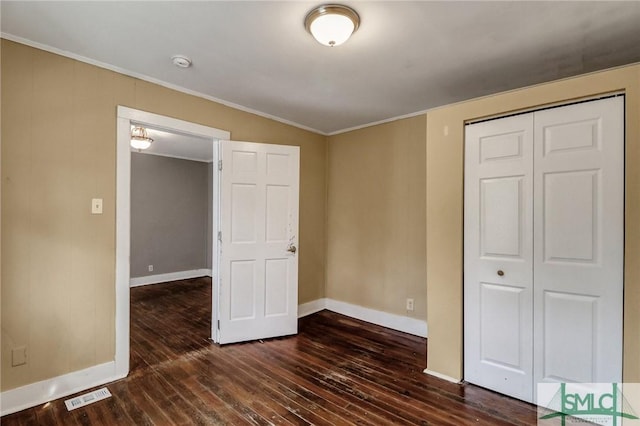 unfurnished bedroom featuring baseboards, visible vents, dark wood-style flooring, ornamental molding, and a closet