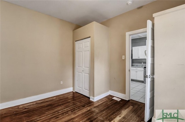 unfurnished bedroom featuring visible vents, baseboards, ensuite bath, and dark wood-style floors