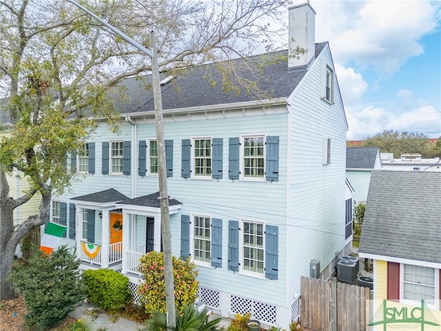 view of front of property featuring central air condition unit, fence, covered porch, a shingled roof, and a chimney