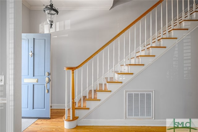 foyer with visible vents, wood finished floors, crown molding, baseboards, and stairs