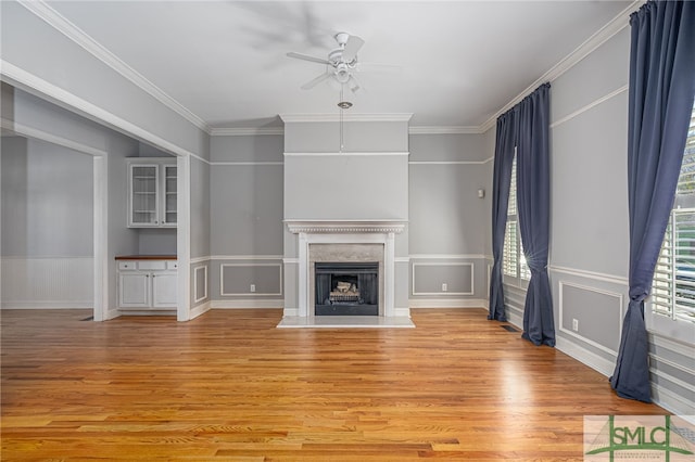 unfurnished living room featuring a fireplace with raised hearth, ceiling fan, crown molding, a decorative wall, and light wood-type flooring