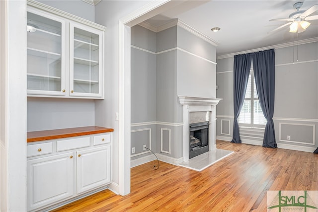 unfurnished living room with light wood-style flooring, a ceiling fan, ornamental molding, a fireplace, and a decorative wall