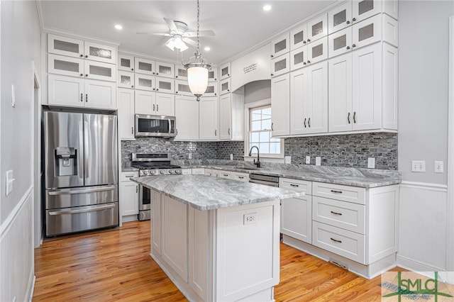 kitchen with stainless steel appliances, a kitchen island, a ceiling fan, and white cabinetry