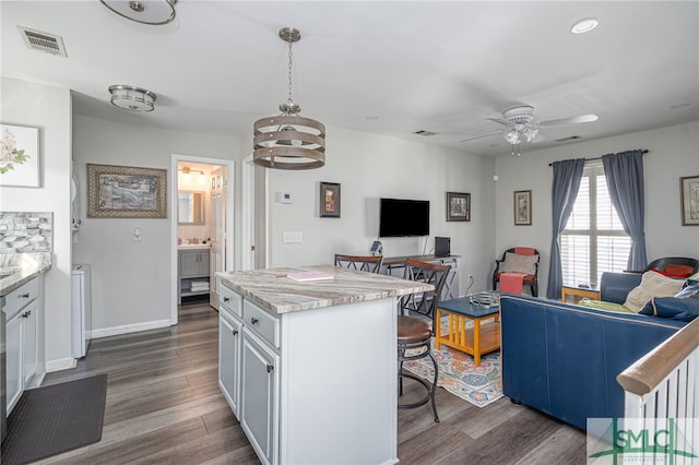 kitchen featuring visible vents, dark wood finished floors, a kitchen bar, ceiling fan with notable chandelier, and open floor plan