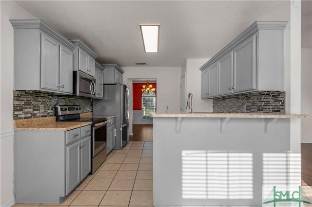 kitchen featuring light tile patterned floors, stainless steel appliances, gray cabinetry, and a peninsula