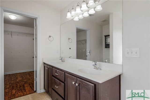 bathroom with double vanity, a walk in closet, and a sink