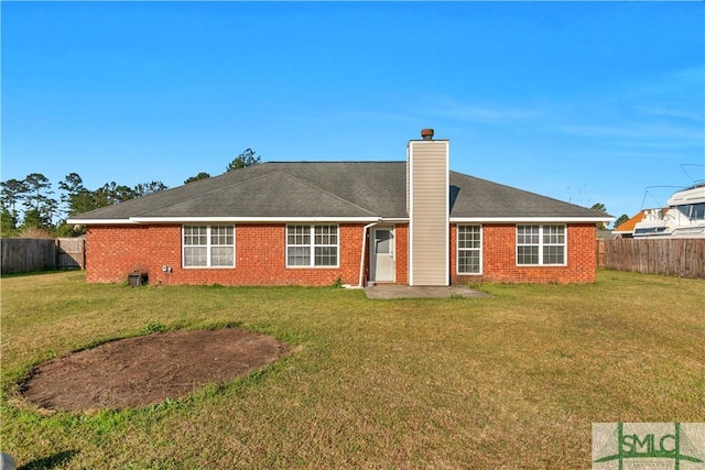 rear view of property with a yard, a chimney, brick siding, and a fenced backyard