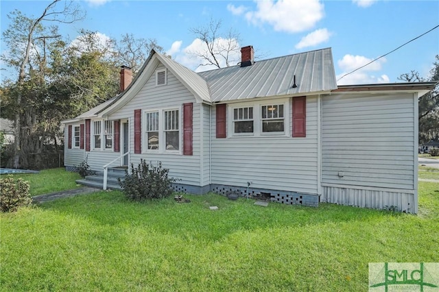 view of front facade featuring entry steps, a front lawn, metal roof, and a chimney