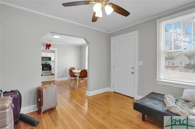 interior space with ornamental molding, a healthy amount of sunlight, arched walkways, and light wood-type flooring