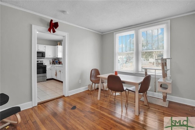 dining area with a textured ceiling, light wood-style flooring, baseboards, and ornamental molding