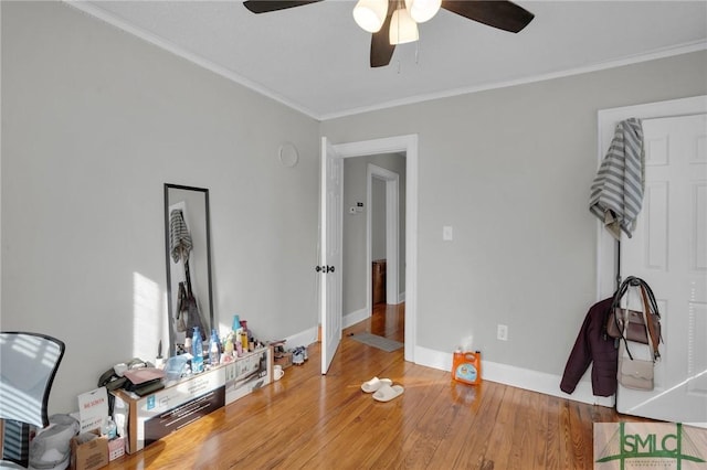 interior space with wood finished floors, a ceiling fan, baseboards, and ornamental molding