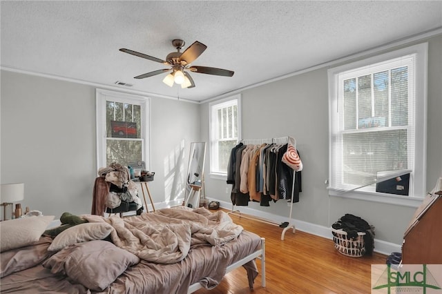 bedroom featuring wood finished floors, baseboards, visible vents, a textured ceiling, and crown molding