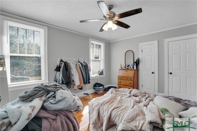 bedroom with a textured ceiling, wood finished floors, baseboards, and ornamental molding