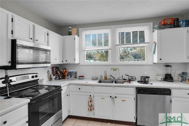 kitchen featuring tasteful backsplash, stainless steel appliances, light tile patterned flooring, white cabinetry, and a sink