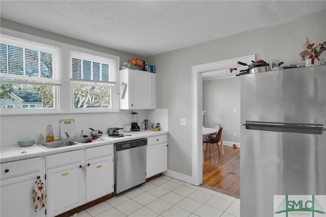 kitchen with a sink, a textured ceiling, white cabinetry, appliances with stainless steel finishes, and light tile patterned flooring