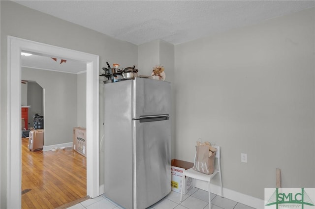 kitchen featuring light tile patterned floors, a textured ceiling, freestanding refrigerator, and baseboards