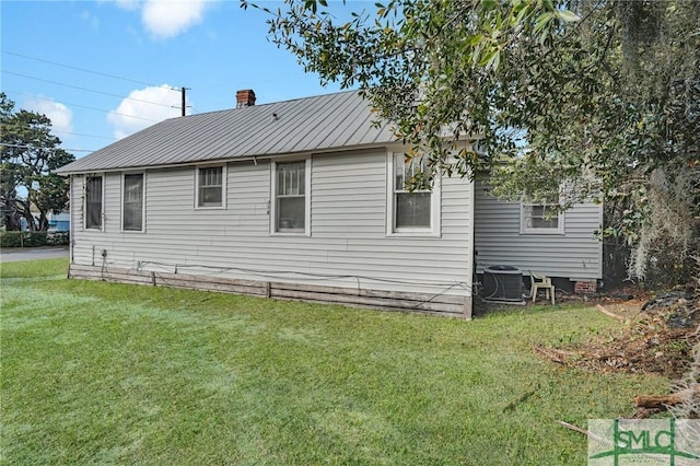 view of side of property with central AC unit, a lawn, a chimney, and metal roof