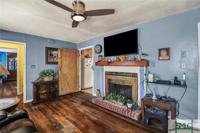 living room with a fireplace with raised hearth, baseboards, a ceiling fan, and wood finished floors