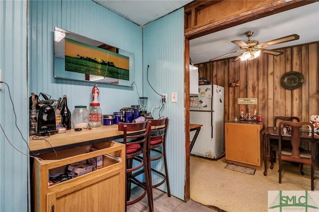 kitchen with wood walls, freestanding refrigerator, a ceiling fan, and tile counters