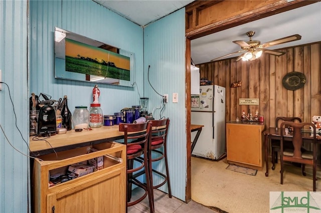 kitchen featuring tile countertops, wooden walls, freestanding refrigerator, and ceiling fan