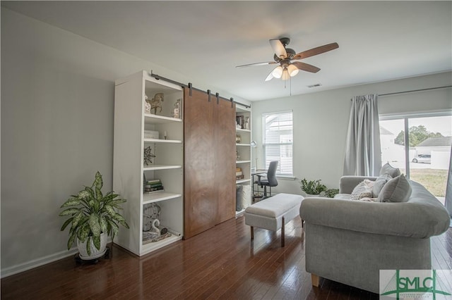 living area with visible vents, a ceiling fan, hardwood / wood-style flooring, a barn door, and baseboards