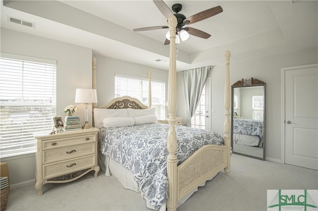 bedroom with visible vents, baseboards, light colored carpet, a tray ceiling, and a ceiling fan