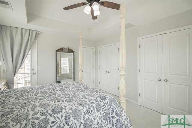 carpeted bedroom featuring baseboards, a ceiling fan, a tray ceiling, and visible vents