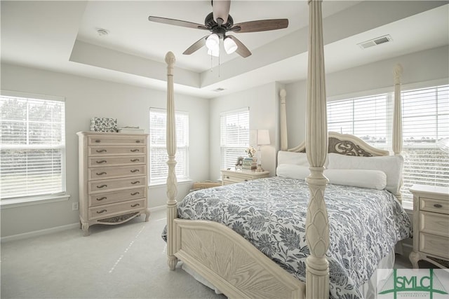 bedroom with visible vents, baseboards, ceiling fan, light colored carpet, and a tray ceiling