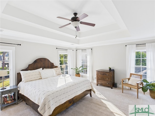 bedroom with a tray ceiling, multiple windows, light colored carpet, and a ceiling fan