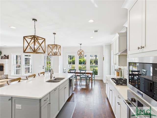 kitchen with an island with sink, a sink, dark wood-style floors, stainless steel appliances, and light countertops