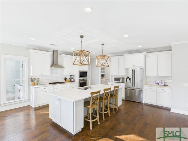 kitchen with dark wood-type flooring, a center island with sink, wall chimney range hood, appliances with stainless steel finishes, and light countertops