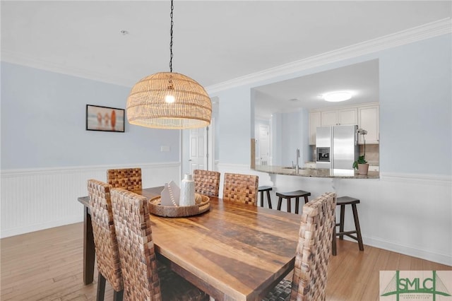 dining space with crown molding, light wood finished floors, and wainscoting