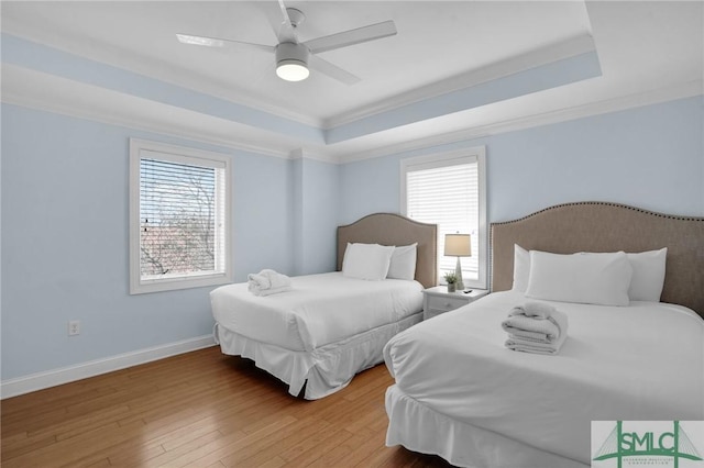 bedroom with ornamental molding, a raised ceiling, baseboards, and hardwood / wood-style flooring