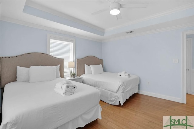 bedroom with wood finished floors, visible vents, baseboards, a tray ceiling, and crown molding