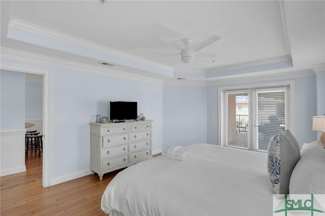 bedroom with visible vents, light wood-style flooring, a tray ceiling, and access to outside