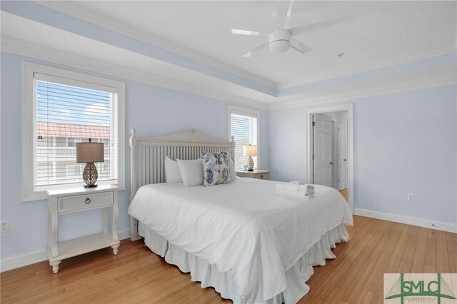 bedroom with a tray ceiling, crown molding, light wood finished floors, baseboards, and ceiling fan