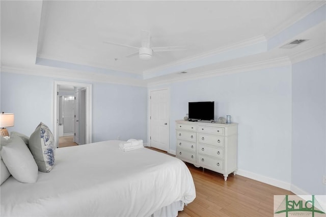 bedroom with light wood-type flooring, a tray ceiling, visible vents, and crown molding