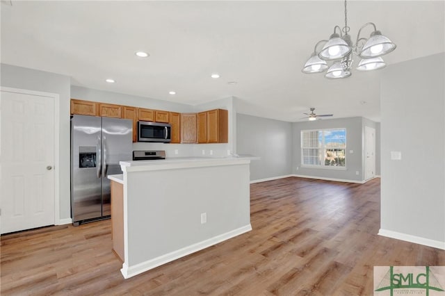 kitchen with light wood-style flooring, ceiling fan with notable chandelier, appliances with stainless steel finishes, light countertops, and baseboards